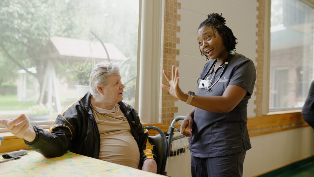 A nurse smiles and talks to a resident at a skilled nursing facility